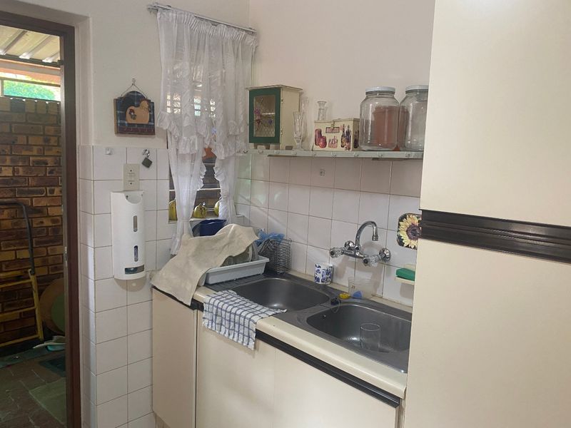A compact scullery area featuring a double stainless steel sink, tiled splashback, and built-in cabinetry, providing a functional secondary prep and wash-up space.