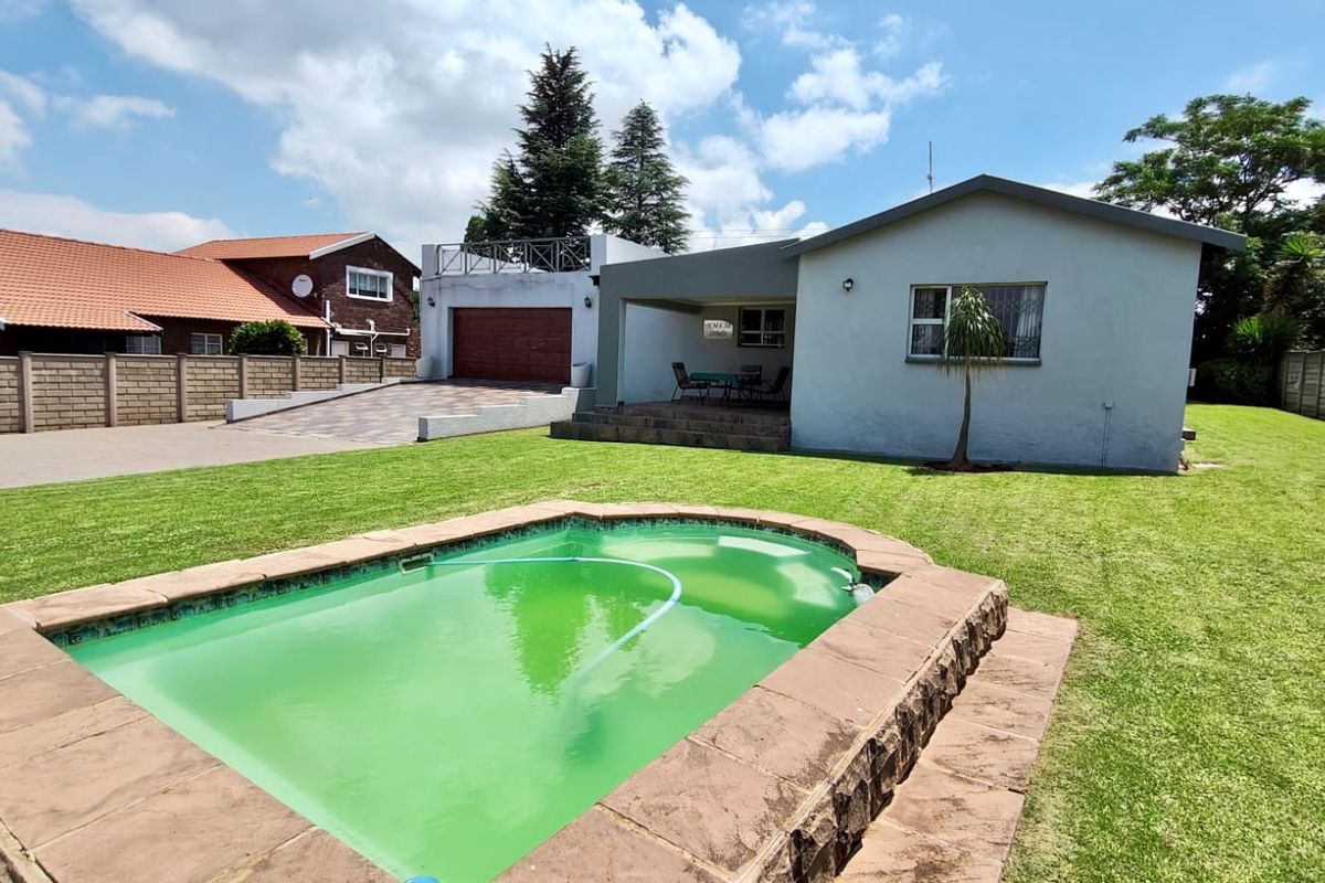 Rear view of the property featuring a swimming pool, paved patio area, lawn, and a detached garage with a paved driveway.
