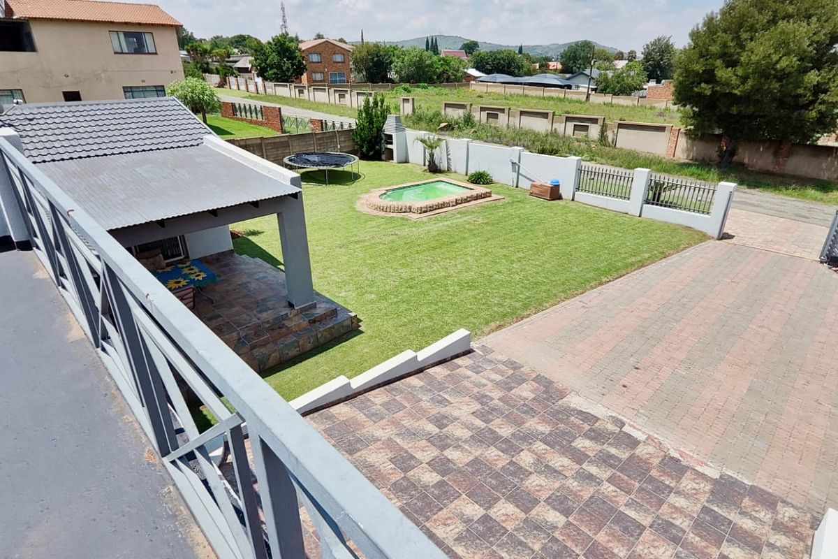Elevated view of the rear garden featuring a swimming pool, covered patio, paved driveway, and perimeter boundary wall.