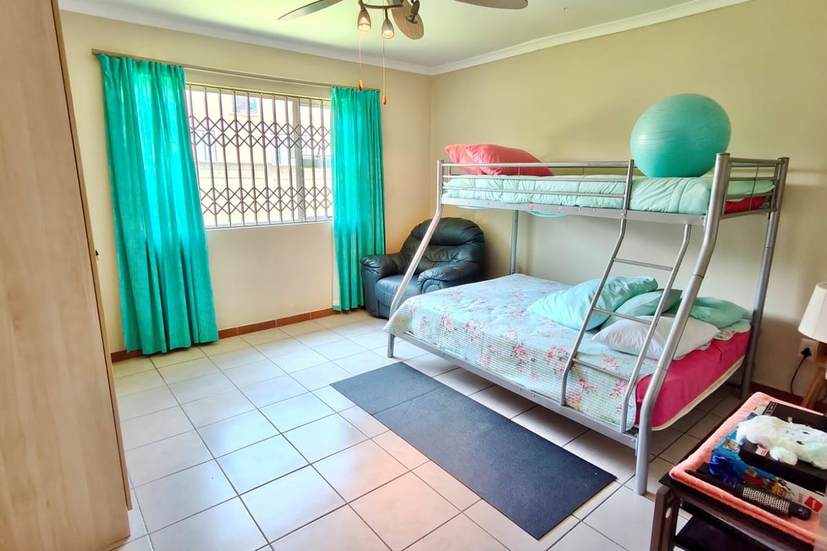 A functional bedroom featuring tiled flooring, a ceiling fan, and security bars on the window, providing a secure and practical living space.