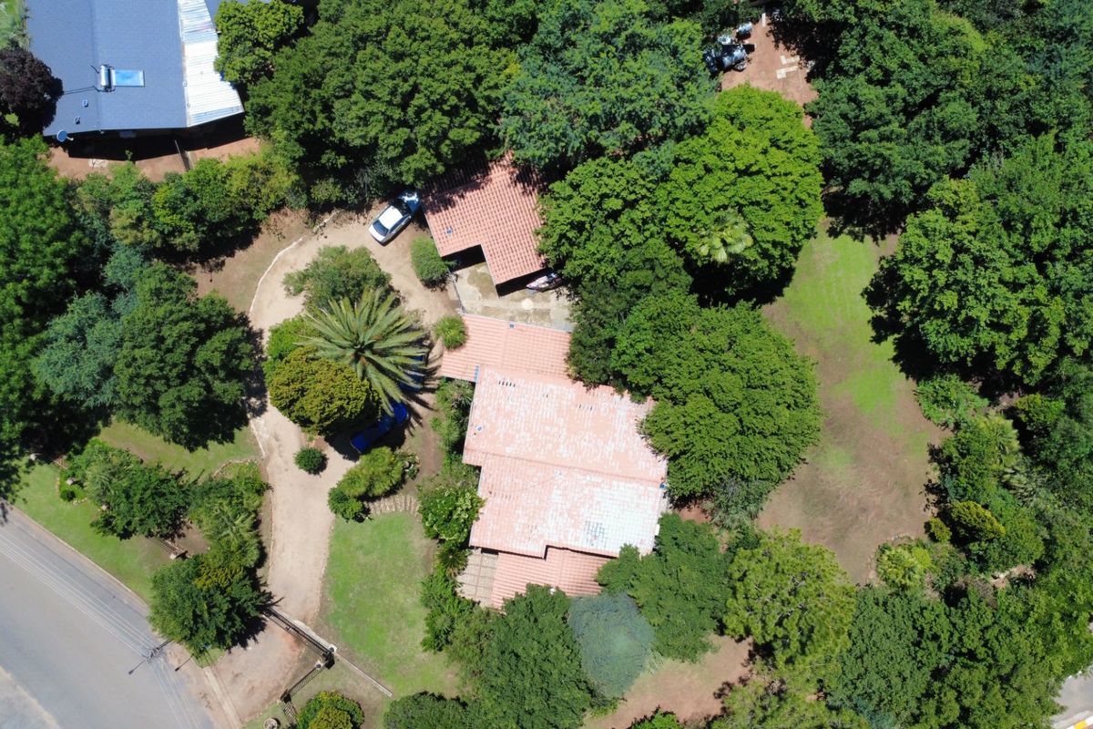 Aerial view of the property showcasing the main dwelling with terracotta roof tiles, surrounded by extensive mature trees and a large garden area.