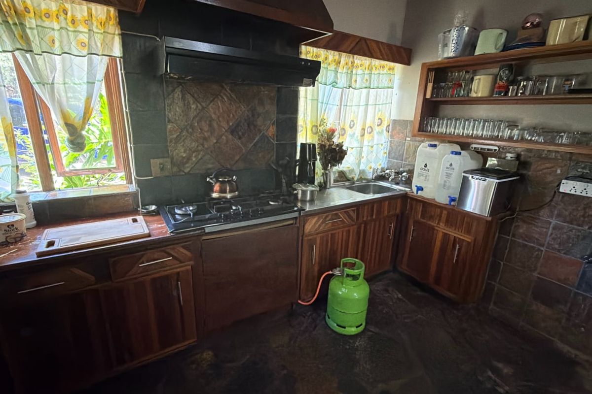 A dated kitchen featuring wooden cabinetry, a gas hob with extractor fan, stone tile backsplash, and open shelving for storage.
