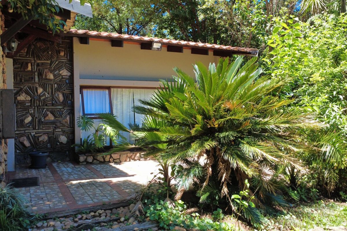 A rear exterior view featuring a stone-clad wall, a tiled patio area, and a covered walkway with exposed timber rafters.