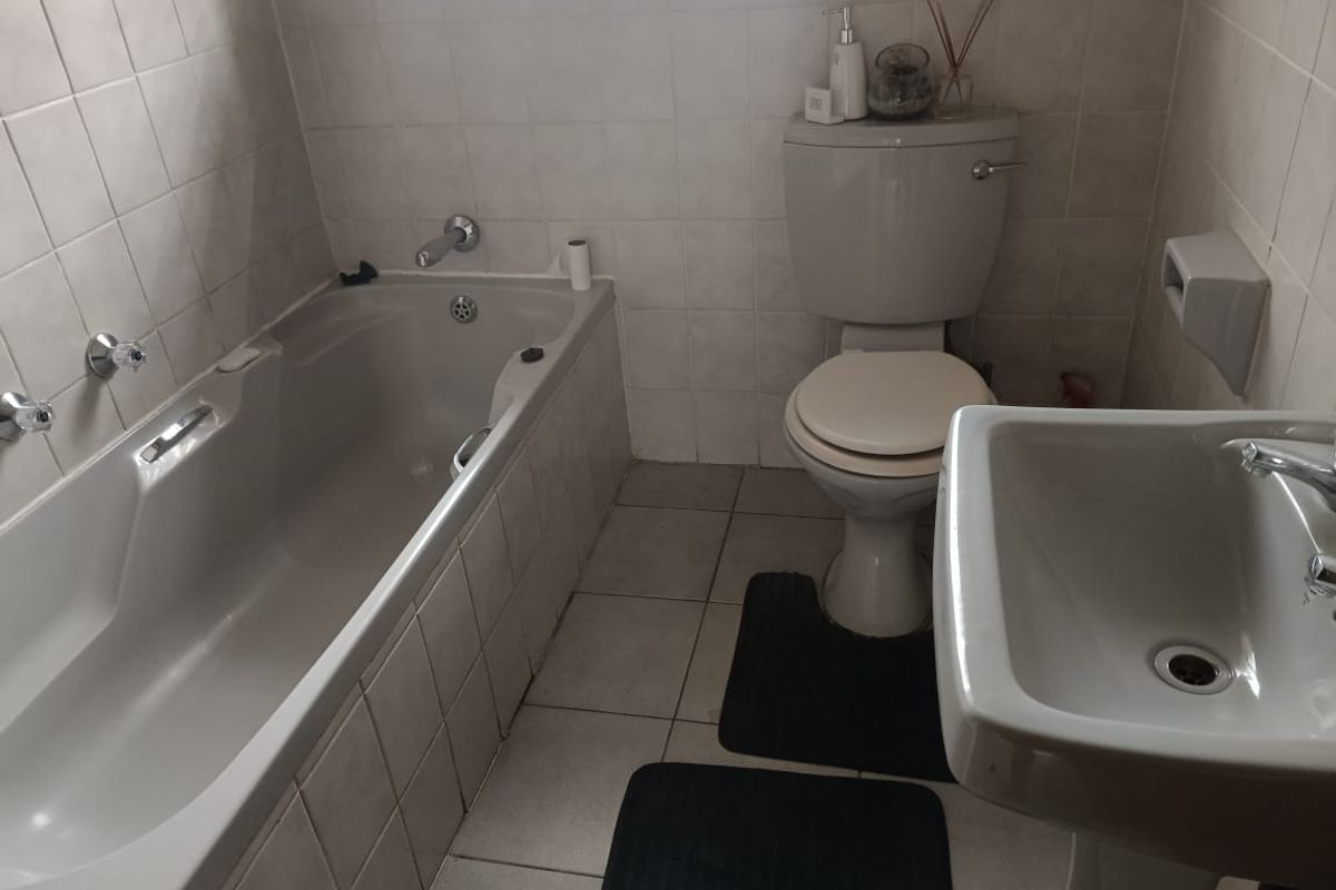 A functional bathroom featuring a built-in bathtub, pedestal washbasin, and toilet with neutral wall and floor tiling.