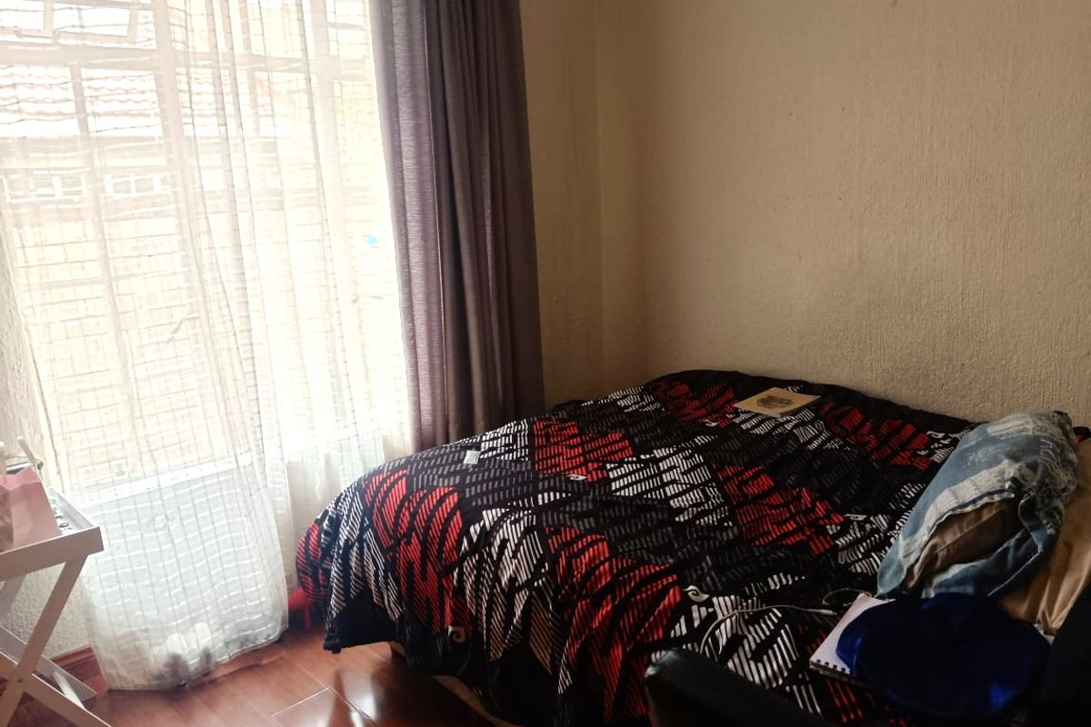 A standard bedroom featuring laminate flooring and large window with curtain tracks, providing natural light.