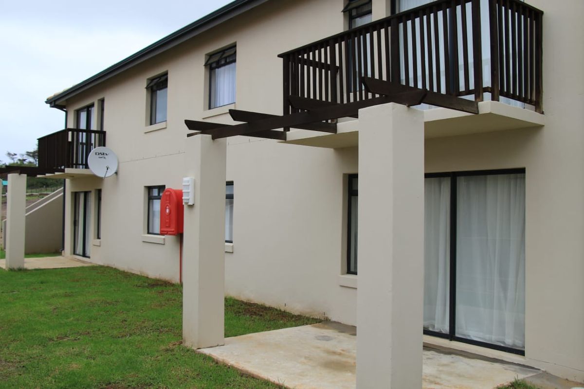 Rear view of the apartment building featuring ground floor patios, upper level balconies with timber pergolas, and sliding door access.