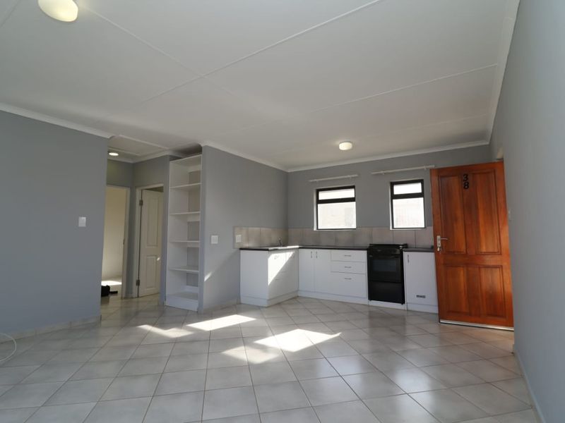 An open-plan living and kitchen area featuring tiled flooring, built-in cabinetry, a stove, and a wooden entrance door in a neutral color palette.