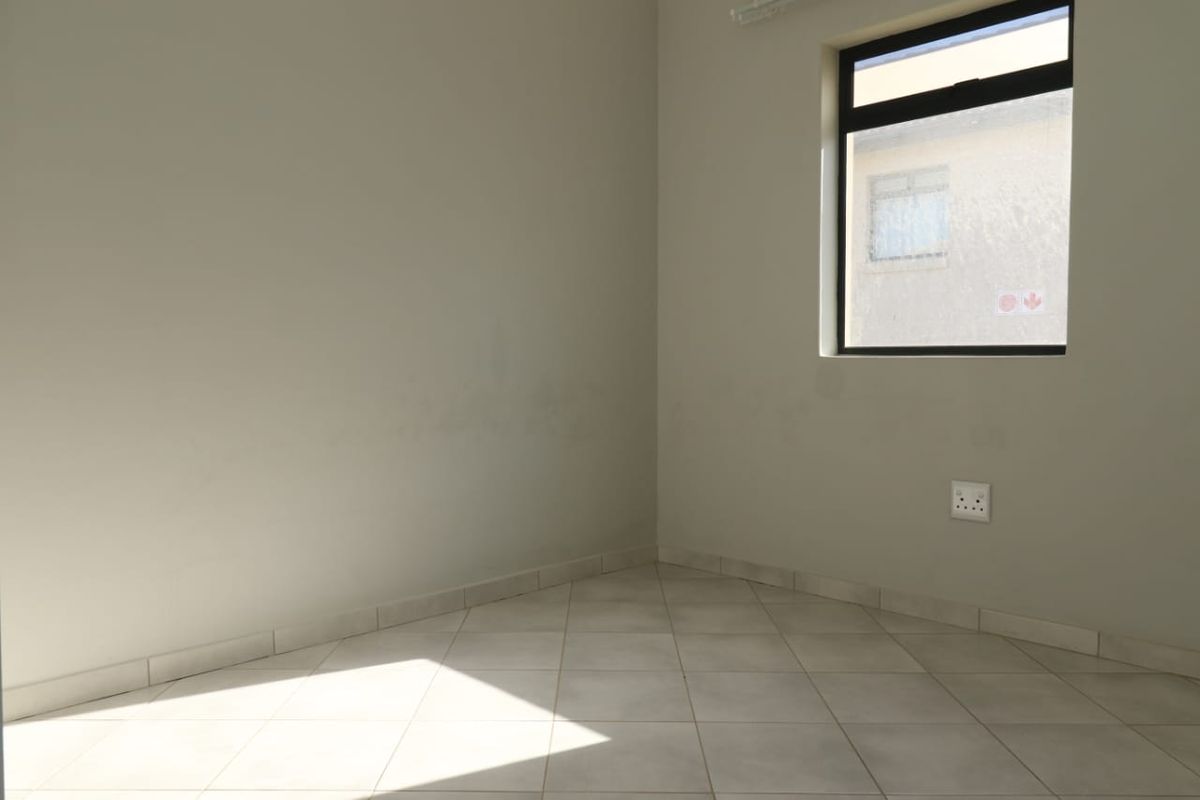 A vacant bedroom featuring neutral tiled flooring, clean wall finishes, and a window providing natural light.