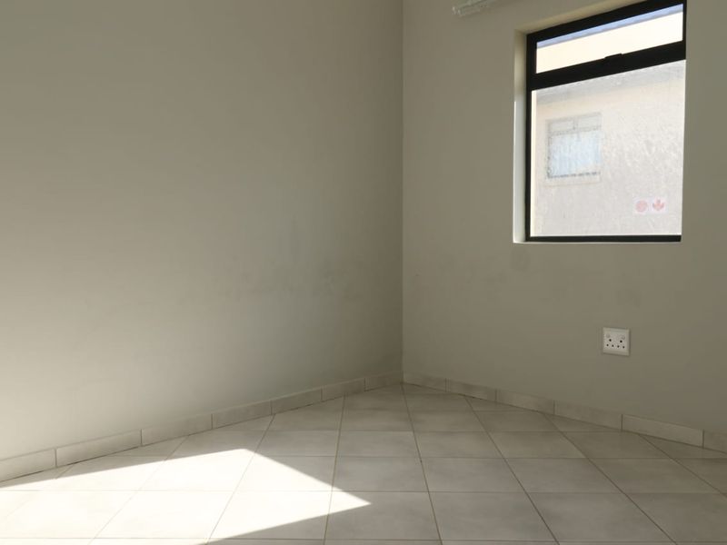 A vacant bedroom featuring neutral tiled flooring, clean wall finishes, and a window providing natural light.