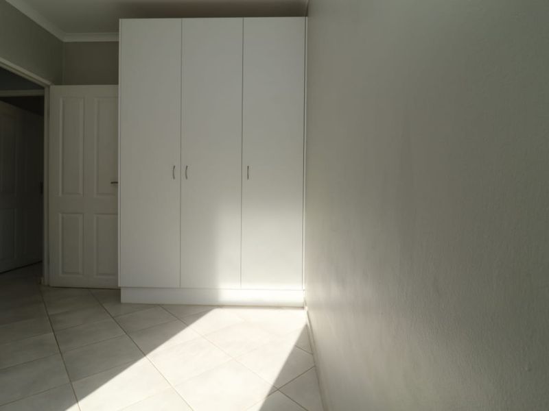A bright, empty bedroom featuring neutral tiled flooring and a clean, white built-in wardrobe.