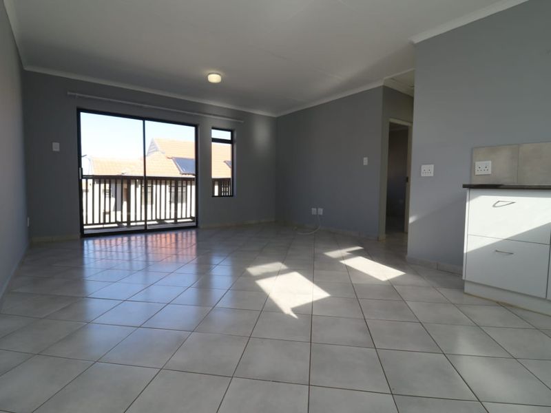 An open-plan living area featuring neutral grey walls, tiled flooring, and direct access to a balcony through a sliding glass door.