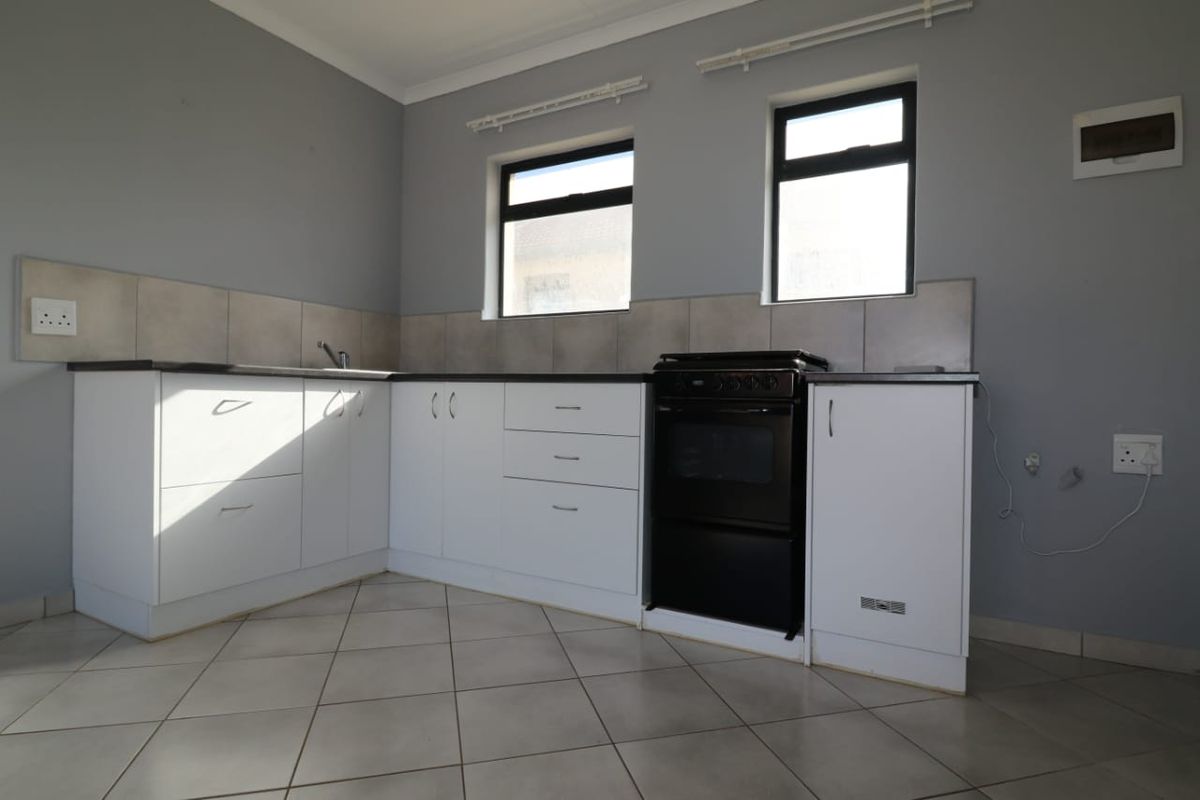 A functional kitchen featuring white cabinetry, tiled backsplash, tiled flooring, and a freestanding stove, offering a clean and neutral space.