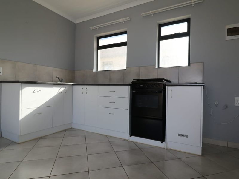 A functional kitchen featuring white cabinetry, tiled backsplash, tiled flooring, and a freestanding stove, offering a clean and neutral space.