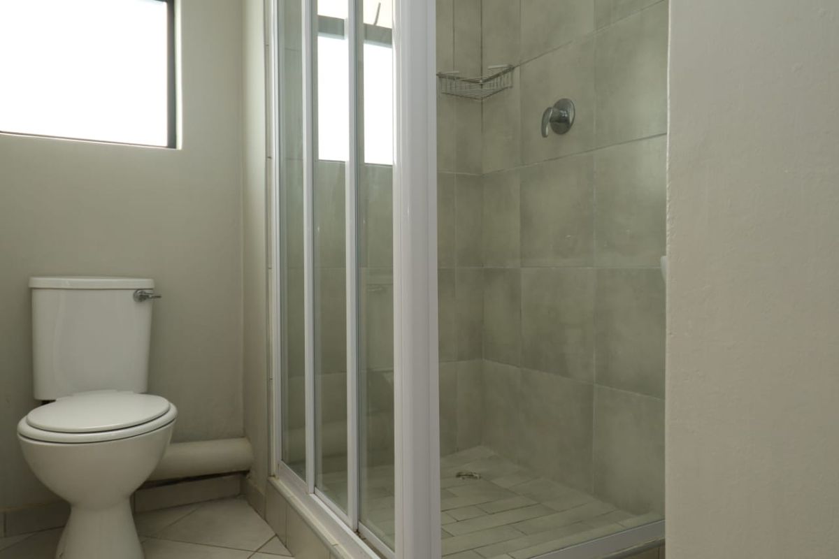 A functional bathroom featuring a shower enclosure with tiled walls and a standard toilet, presenting a clean but dated aesthetic.
