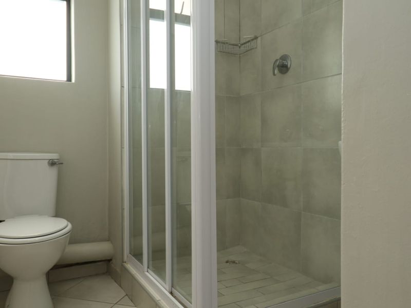 A functional bathroom featuring a shower enclosure with tiled walls and a standard toilet, presenting a clean but dated aesthetic.