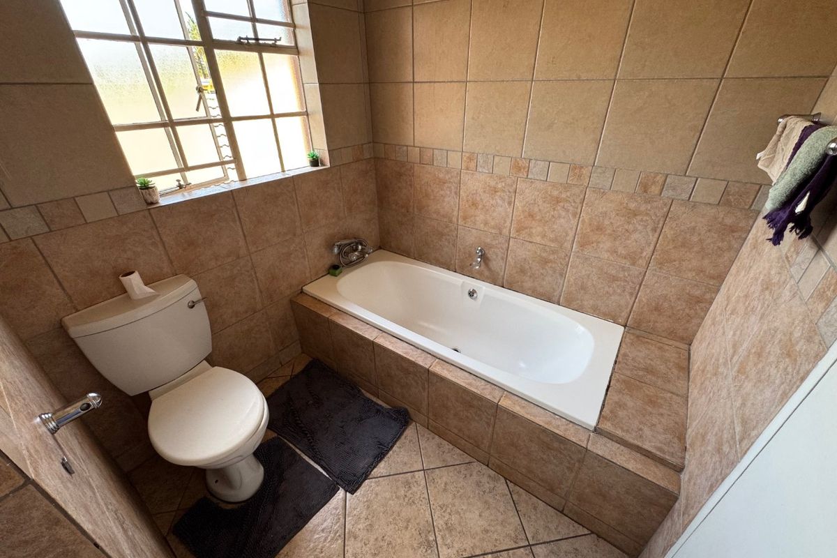 A functional bathroom featuring a built-in bathtub with tiled surround, a standard toilet, and a window providing natural light.