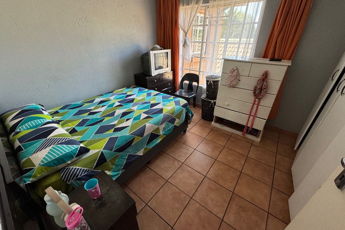 A bedroom featuring tiled flooring, a large window with security bars, and built-in cupboard space.