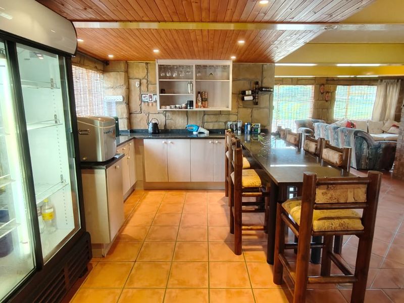 Open plan kitchen and dining area featuring timber ceilings, stone wall accents, tiled flooring, and a built-in breakfast bar.