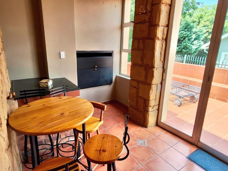 Covered patio area featuring a built-in braai, stone-clad pillars, and tiled flooring, with direct access to an outdoor terrace through sliding glass doors.