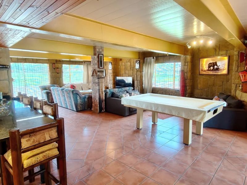 Spacious open-plan living and entertainment area featuring stone-clad walls, tiled flooring, and a timber-paneled ceiling, offering a rustic and versatile layout.