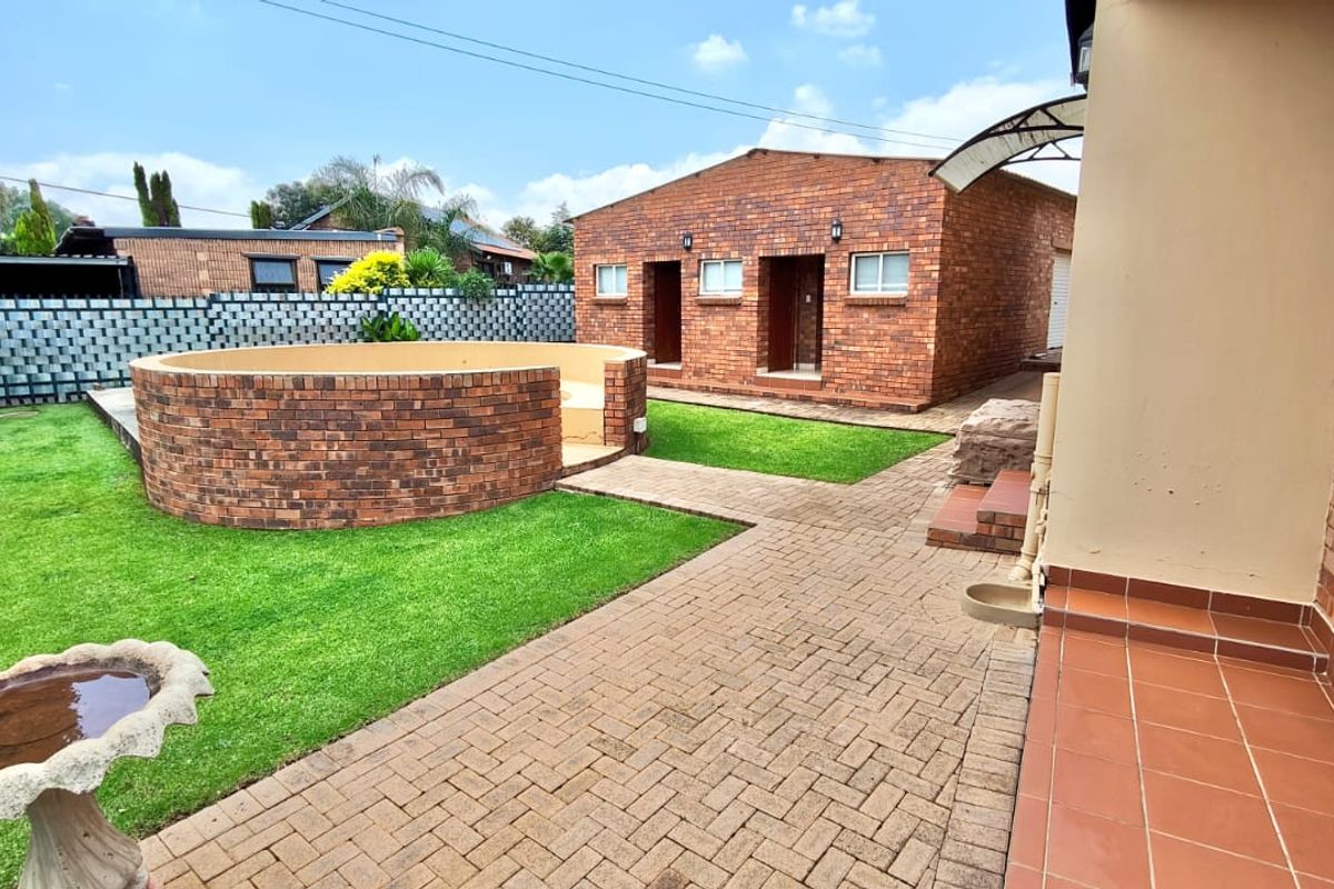 A well-maintained rear garden featuring a paved walkway, a raised circular brick planter, and a detached brick outbuilding.