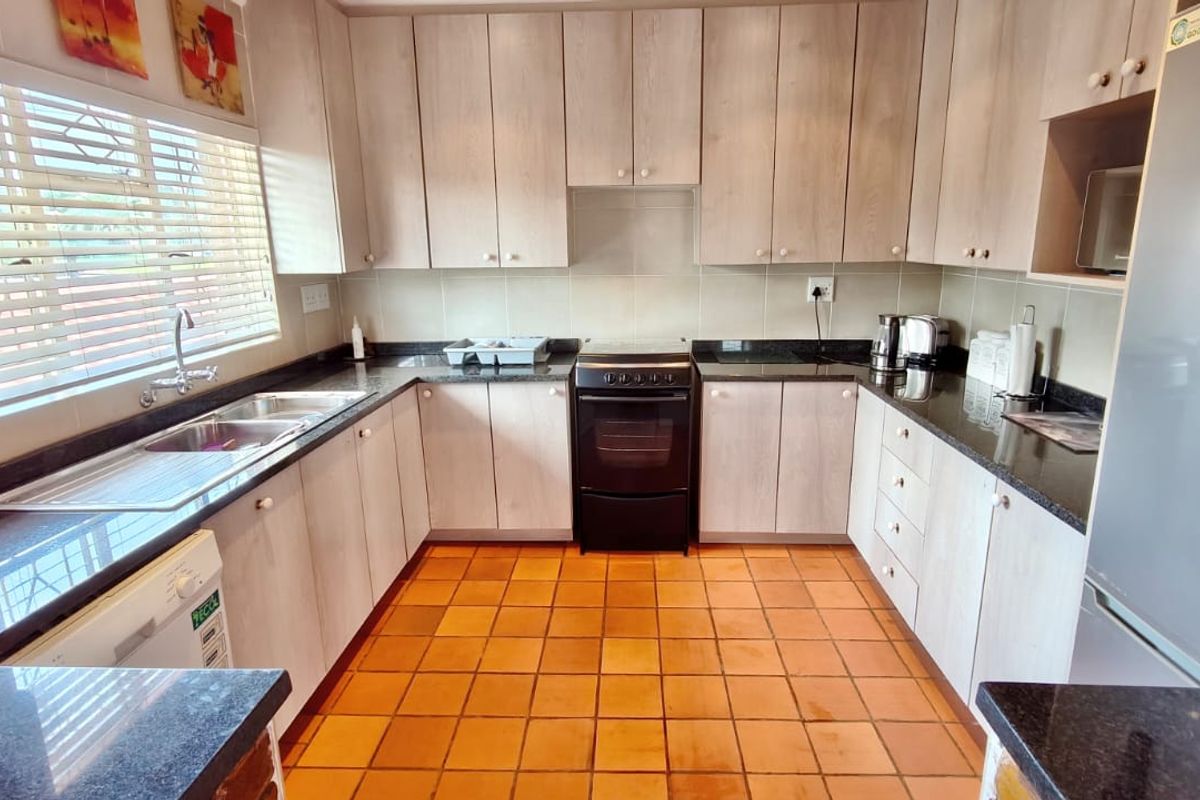A functional U-shaped kitchen featuring light wood-tone cabinetry, dark granite countertops, a double basin sink, and a freestanding oven with tiled flooring.