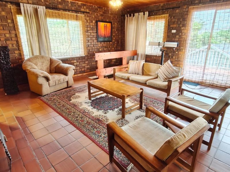 A spacious living room featuring exposed brick walls, tiled flooring, a timber ceiling, and a built-in fireplace with access to an outdoor area.