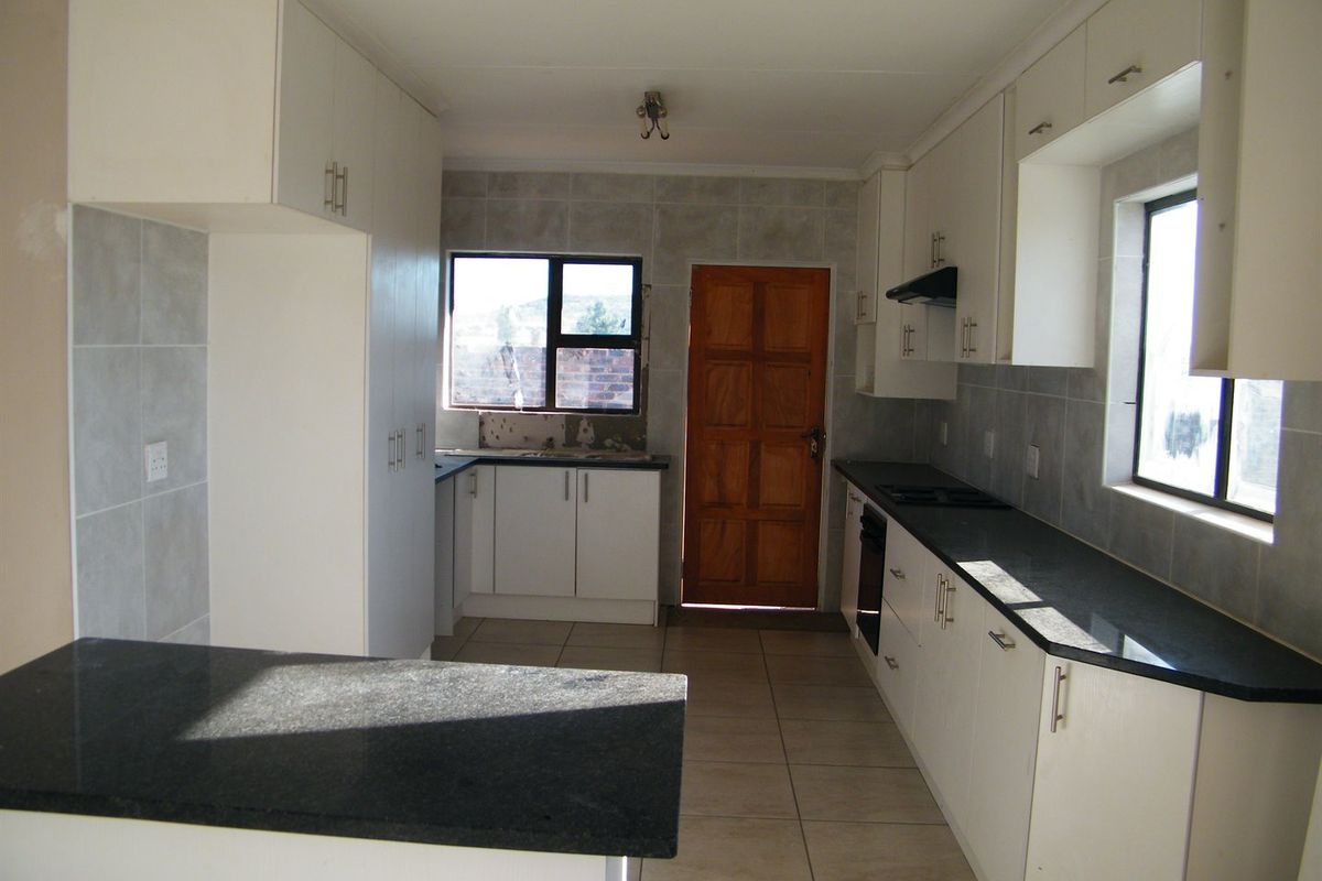 A functional kitchen featuring white cabinetry, dark granite countertops, tiled flooring, and a built-in oven with an extractor fan.