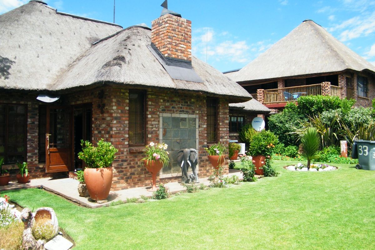 Rear view of a charming thatch-roofed house featuring exposed brickwork, a brick chimney, and a well-maintained garden with a paved patio area.