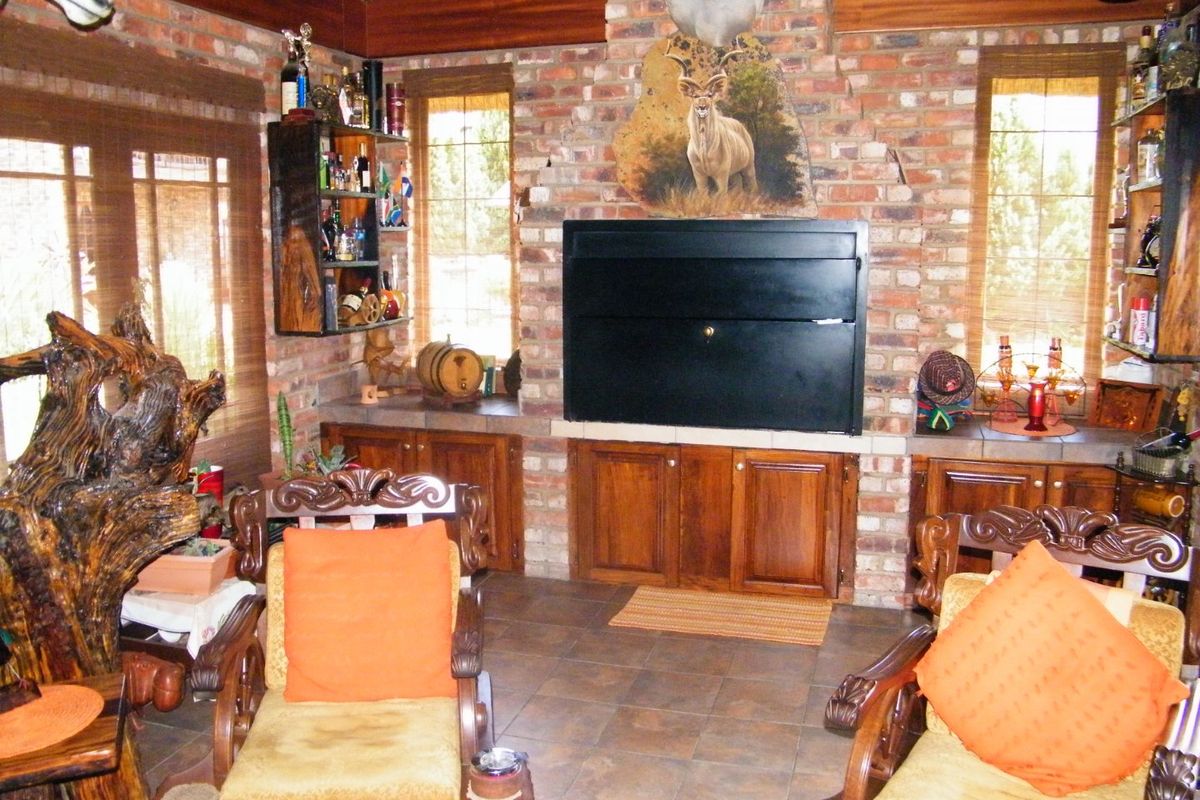 A rustic living room featuring exposed brick walls, a built-in fireplace with cabinetry, tiled flooring, and a traditional thatched ceiling.