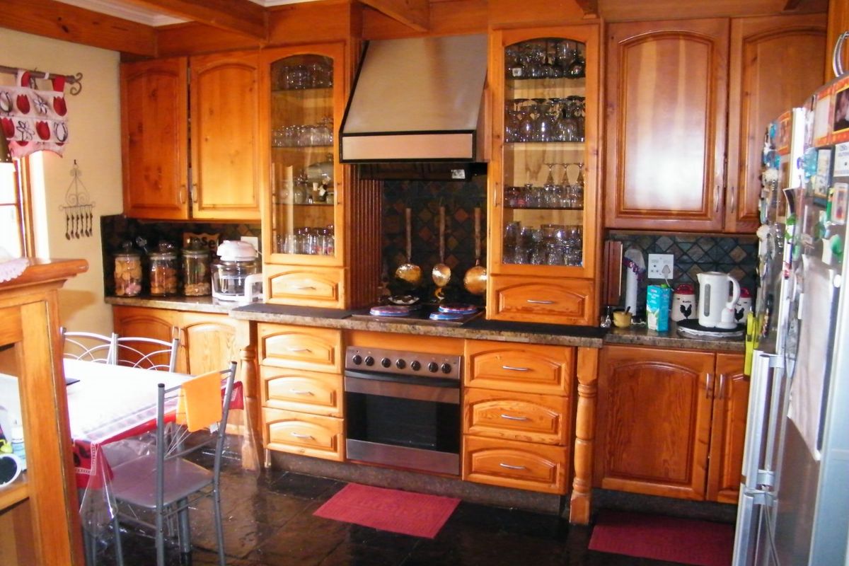 A traditional kitchen featuring extensive timber cabinetry, stone countertops, built-in oven with extractor fan, and dark stone flooring with exposed timber ceiling beams.