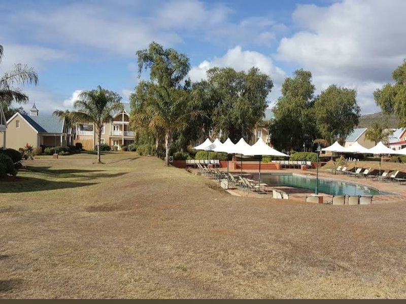 A view of a residential complex featuring a swimming pool area with paved decking and surrounding landscaped gardens.