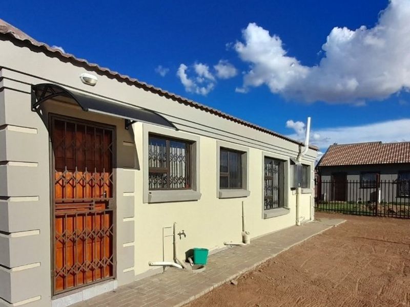 Rear exterior view of the house featuring a paved walkway, security gate, and external plumbing fixtures against a clean rendered facade.