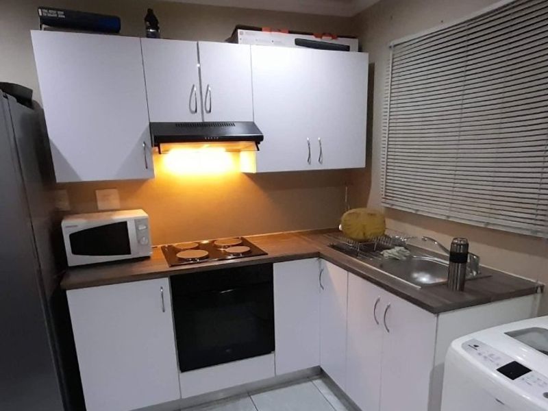 Compact kitchen featuring white cabinetry, laminate countertops, integrated oven, electric hob, extractor fan, and a stainless steel sink with tiled flooring.