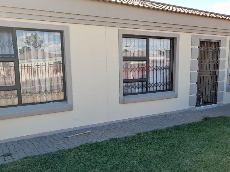 Front exterior view of the house featuring a tiled roof, aluminium window frames with security bars, and a paved walkway alongside a neat lawn.