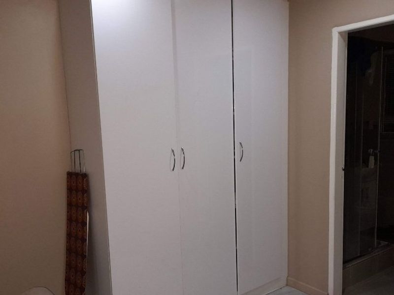 A bedroom featuring a modern white built-in wardrobe with sleek handles, providing ample storage space.