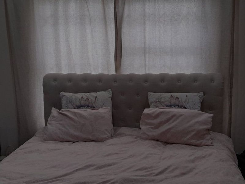 A dimly lit bedroom interior featuring a tufted headboard against a window with curtains.
