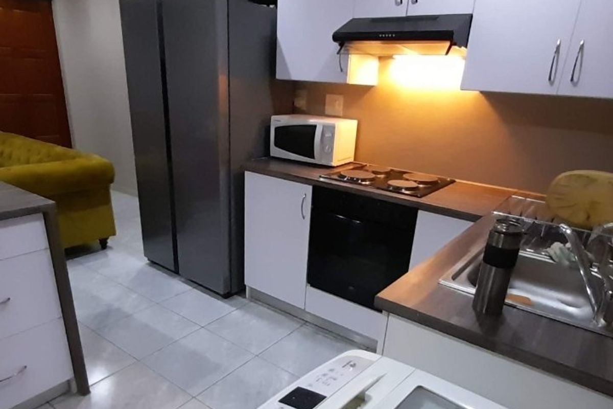 A functional kitchen featuring modern white cabinetry, integrated appliances including an oven and hob, and tiled flooring.