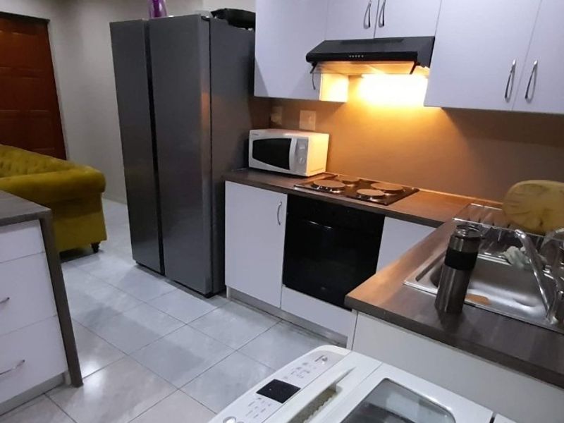 A functional kitchen featuring modern white cabinetry, integrated appliances including an oven and hob, and tiled flooring.