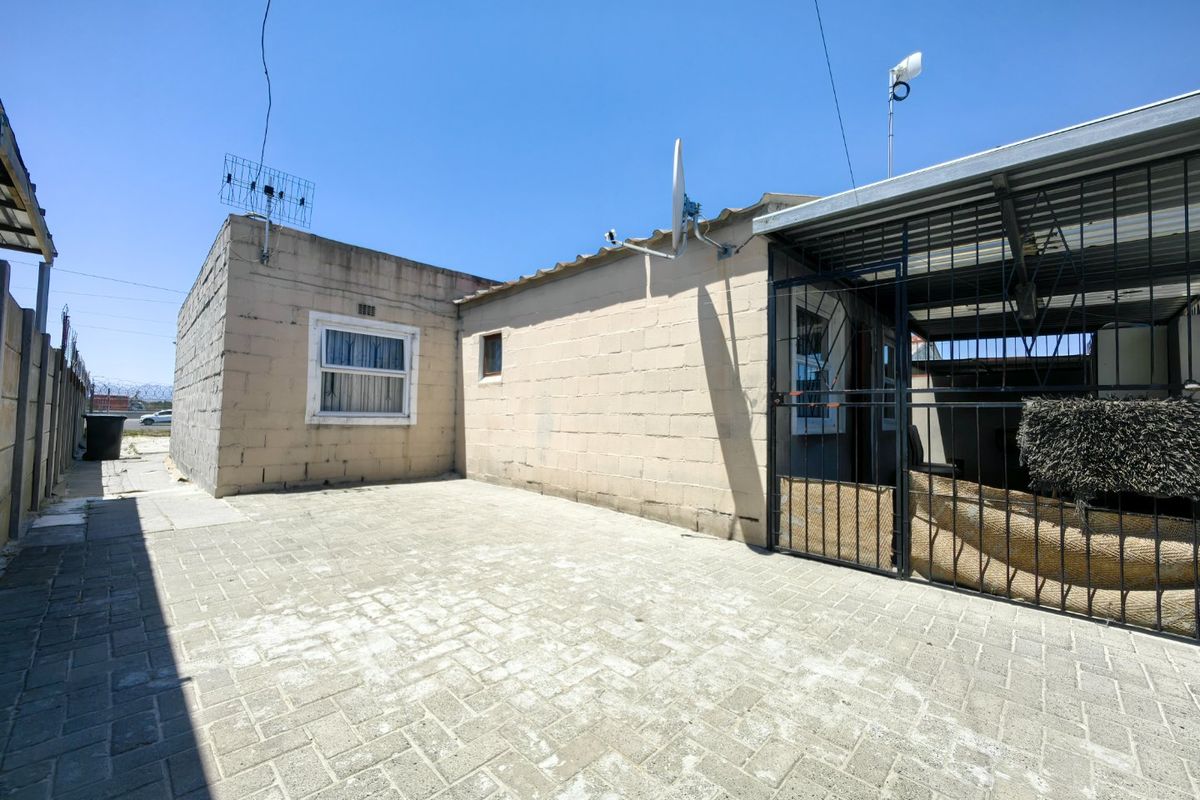 Rear exterior view of the property featuring a paved courtyard, concrete block walls, and a covered metal structure with security gate.