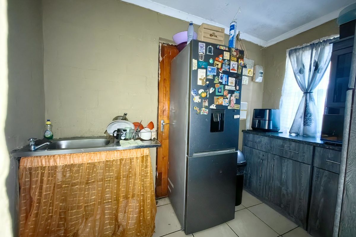 A functional kitchen area featuring a stainless steel sink, built-in cabinetry, and tiled flooring, currently showing signs of wear and dated finishes.