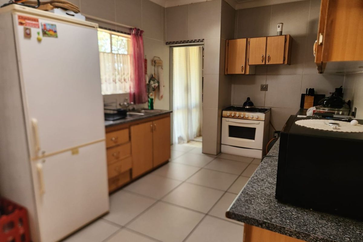 A functional kitchen featuring tiled flooring, wooden cabinetry, a freestanding stove, and a double sink with a window view.