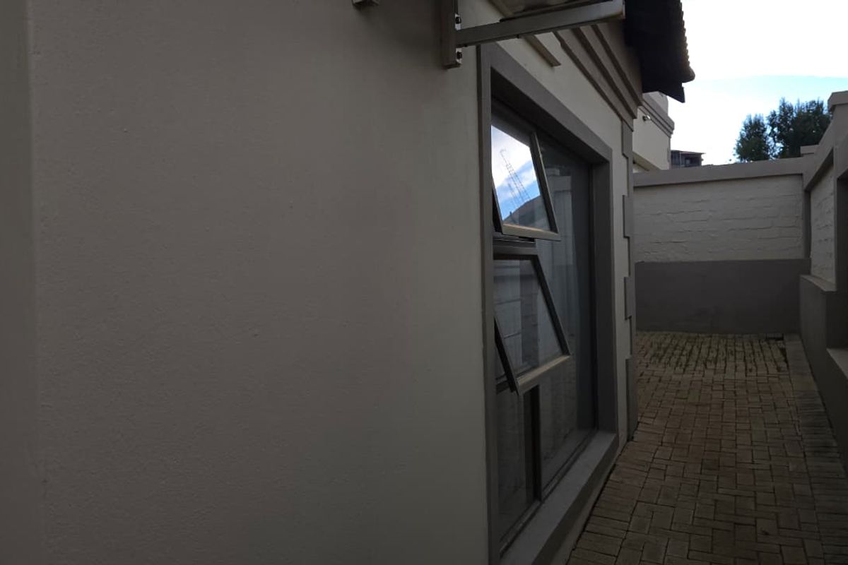 A side exterior view of the townhouse featuring paved pathways, boundary walls, and modern window frames.