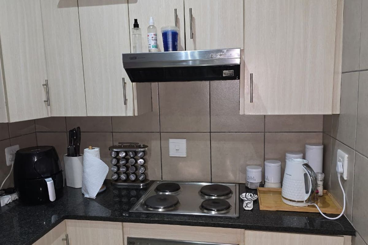 A functional kitchen area featuring light-toned cabinetry, a dark granite countertop, a stainless steel electric hob, and a built-in extractor fan.
