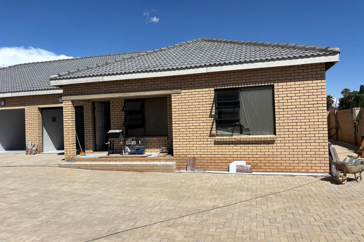 Front elevation of a face brick townhouse featuring a tiled roof, paved driveway, and covered entrance area, currently undergoing minor exterior finishing work.