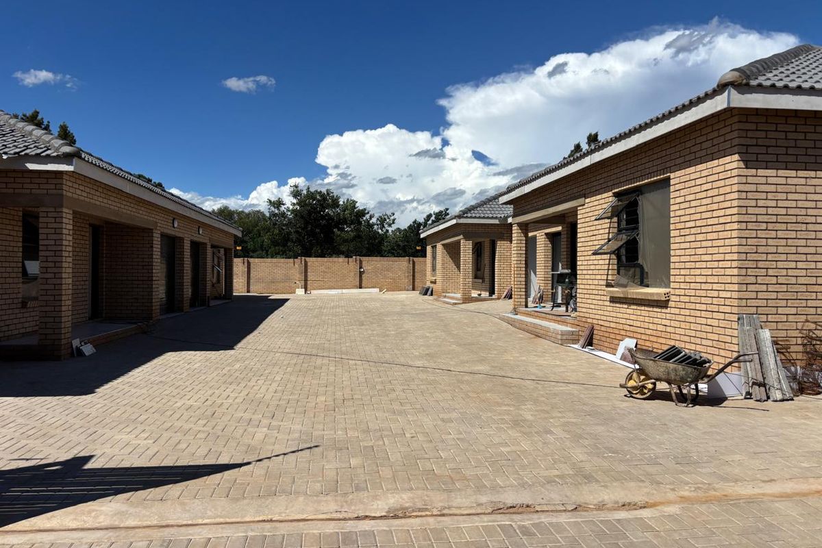 Exterior view of a townhouse complex featuring face brick construction, tiled roofs, and a large paved driveway area under development.