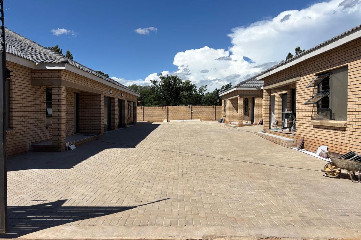 A view of the paved driveway and front facades of the townhouse units, featuring face brick construction and tiled roofing.