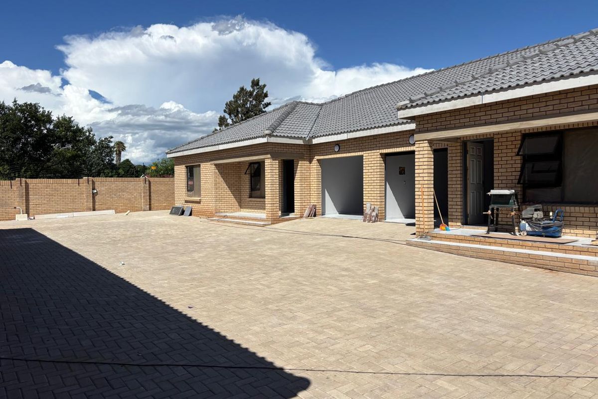 A view of the front exterior of a face brick townhouse featuring a large paved driveway, double garage, and perimeter walling.