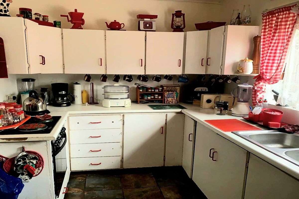 A dated kitchen featuring white built-in cabinetry, laminate countertops, a stainless steel double sink, and tiled flooring.