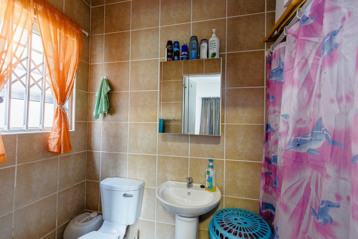 A functional bathroom featuring tiled walls, a pedestal basin, and a built-in medicine cabinet with security bars on the window.